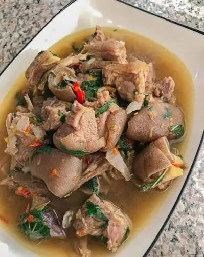 Halal boneless goat pepper soup with uziza leaves and sliced red chilli in a white serving dish